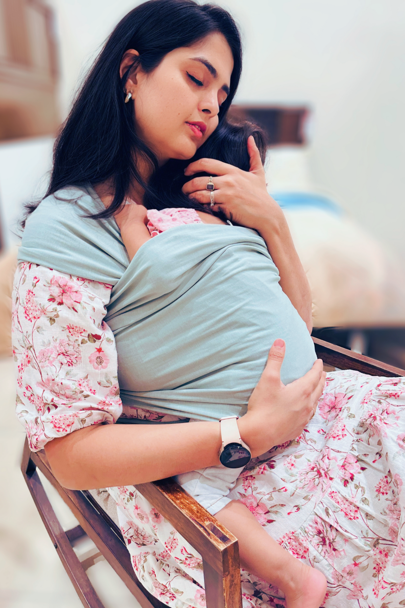 A mother comforting a child in kangaroo wrap on a rocking chair.